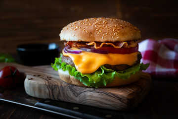 Burger with cheese, bacon, tomato and lettuce on dark wooden background