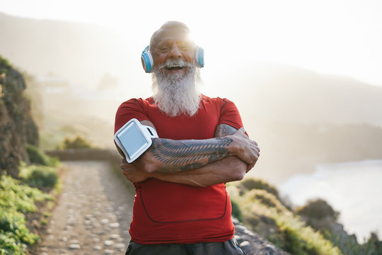 Senior fit man outdoor after workout joggin session - Mature athlete training outside while listening playlist music with headphones - Sport and joyful elderly lifestyle concept