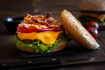 Burger with cheese, bacon, tomato and lettuce on dark wooden background