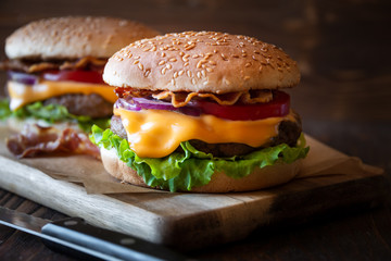 Burger with cheese, bacon, tomato and lettuce on dark wooden background