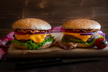 Burger with cheese, bacon, tomato and lettuce on dark wooden background