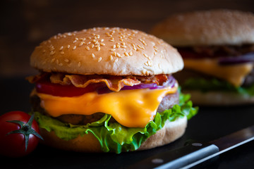 Burger with cheese, bacon, tomato and lettuce on dark wooden background
