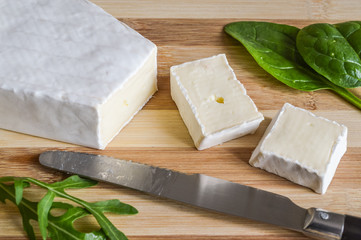 slices of brie cheese on wood cutting board with green salad leaves close up