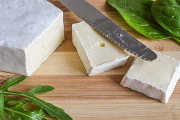 slices of brie cheese on wood cutting board with green salad leaves close up