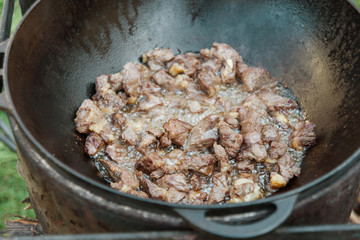 Pilaf Cooking in cauldron on fire outdoors series. Pieces of lamb meat are fried in boiling oil in pan on fire. step-by-step process of cooking pilaf. takeaway food and service concept. Kazan on grill