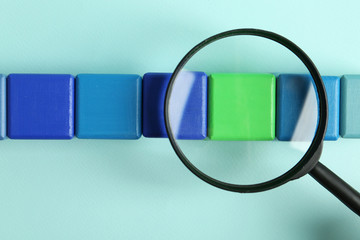 Magnifying glass and colorful cubes on light blue background, top view. Search concept