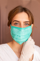 portrait of beautiful young woman wearing cotton green mask and white medical/surgical gloves on pastel background. 