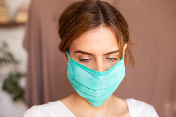 portrait of beautiful young woman wearing cotton green mask and white medical/surgical gloves on pastel background. 
