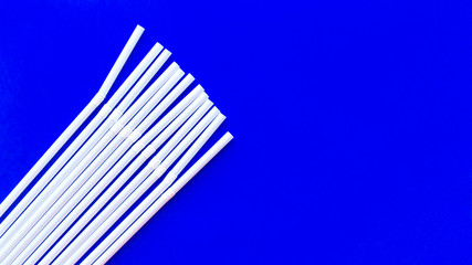 Scattered white plastic tubules for juice and cocktails on a blue background. Disposable straws. The subject of serving. Bar accessories. Summer planet pollution concept.