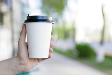 Paper coffee cup in woman's hand with blur background bokeh