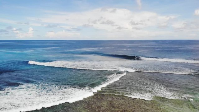 Slow tracking drone view of a shallow area on a popular surfing beach in the Maldives; sunny day, partly cloudy sky.