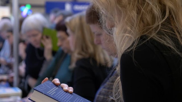 Blond hair woman with glasses furiously searching for intresting book in Book Fair
