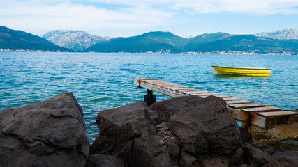 Rocky coast with wooden jetty towards beautiful mountains and sea with a yellow boat on it