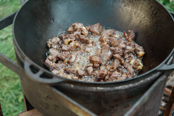 Pilaf Cooking in cauldron on fire outdoors series. Pieces of lamb meat are fried in boiling oil in pan on fire. step-by-step process of cooking pilaf. takeaway food and service concept. Kazan on grill