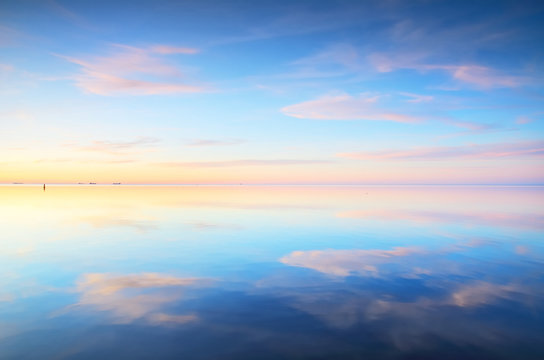 Panoramic view of the snow-covered shore of the frozen Saima lake at sunset. Stunning pink cloudscape. Symmetry reflections on the water. Winter wonderland. Finland