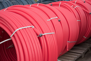 Fototapeta premium Red plastic pipes rolled into open air rolls. Construction site