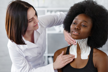 Kinesiology taping. Physiotherapist applying kinesiology tape to patient neck. Therapist treating young female African American athlete. Post traumatic rehabilitation, sport physical therapy. - obrazy, fototapety, plakaty