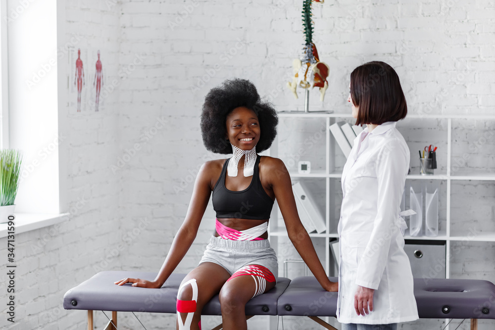 Poster Young female African American athlete visiting physiotherapist. Kinesiology taping. Anti-cellulite procedure, fat lose, cellulite removal, post traumatic rehabilitation,sport physical therapy.