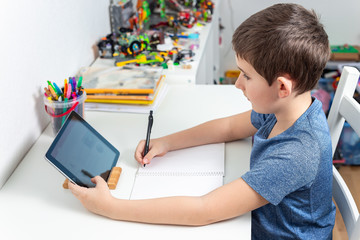 Homeschooling at isolation, eight years old boy behind the table study at home using a tablet, digital education