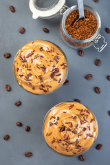 Dalgona coffee with ice garnished with grated chocolate, trendy korean drink on a dark gray background, vertical, top view,  closeup