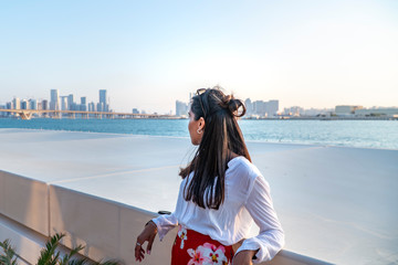Fototapeta na wymiar Woman & Abu Dhabi Cityscape skyline, with buildings, river water and skyscrappers. Tourist on holiday looking at city. Vacation, Tourism shot. Beautiful Emirates City at dusk. 