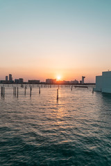 Fototapeta premium Abu Dhabi Cityscape SUNSET skyline, with buildings, river water and skyscrappers. Beautiful Emirates City at dusk. Orange sun.