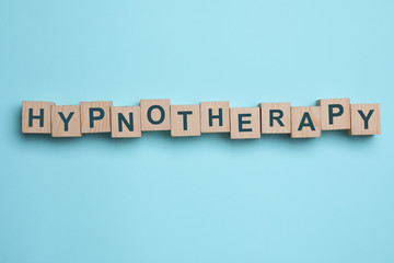 Wooden blocks with word HYPNOTHERAPY on light blue background, flat lay