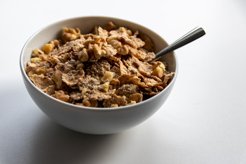 Porzellanschüssel mit gesundem Müsli, Cornflakes, Walnüssen und Löffel ist bereit fürs Frühstück mit Cerealien, Cornflakes und Müsli als gesunde Mahlzeit und Ernährung am Frühstückstisch