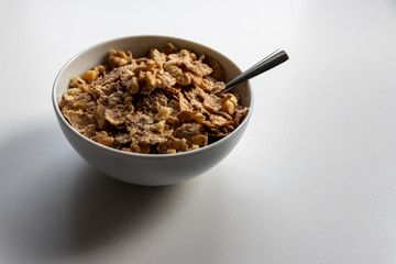 Porzellanschüssel mit gesundem Müsli, Cornflakes, Walnüssen und Löffel ist bereit fürs Frühstück mit Cerealien, Cornflakes und Müsli als gesunde Mahlzeit und Ernährung am Frühstückstisch