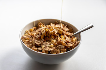 Schüssel mit gesundem Müsli, Cornflakes, Walnüssen, Honig und Löffel ist bereit fürs Frühstück mit Cerealien, Cornflakes und Müsli als gesunde Mahlzeit und Ernährung am Frühstückstisch