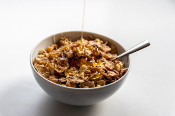 Schüssel mit gesundem Müsli, Cornflakes, Walnüssen, Honig und Löffel ist bereit fürs Frühstück mit Cerealien, Cornflakes und Müsli als gesunde Mahlzeit und Ernährung am Frühstückstisch