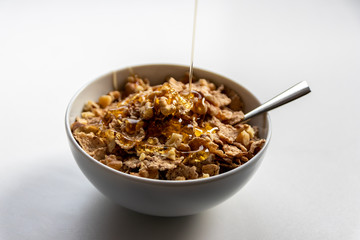 Schüssel mit gesundem Müsli, Cornflakes, Walnüssen, Honig und Löffel ist bereit fürs Frühstück mit Cerealien, Cornflakes und Müsli als gesunde Mahlzeit und Ernährung am Frühstückstisch