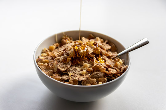 Sch&uuml;ssel mit gesundem M&uuml;sli, Cornflakes, Waln&uuml;ssen, Honig und L&ouml;ffel ist bereit f&uuml;rs Fr&uuml;hst&uuml;ck mit Cerealien, Cornflakes und M&uuml;sli als gesunde Mahlzeit und Ern&auml;hrung am Fr&uuml;hst&uuml;ckstisch