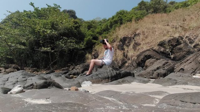 A Male Tourist Sitting On The Rock Remove The Controller On His Head Before Walking Away On The Shore In Phi Phi Islands, Thailand On A Summer Day - Medium Shot