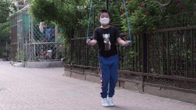 Chinese kid with face mask jumping rope outdoor in corona virus pandemic.
