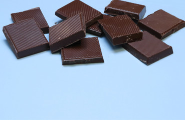 a bar of dark chocolate is broken into pieces, lies on a blue background. Place for text,...