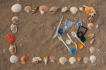 Plastic waste: bags, disposable plastic appliances, plastic lids on the sand in a shell frame. Concept of ecology, environmental pollution, environmental purification,nature conservation, stop plastic