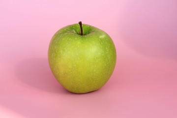 Green yellow apple on a pink background. Juicy ripe beautiful fruit.