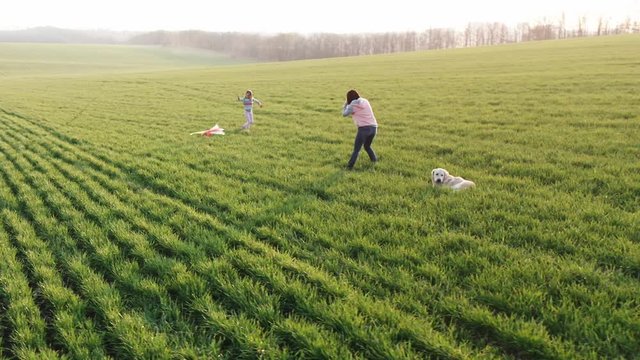 Pretty woman shooting cute little girl with kite on field at sunset