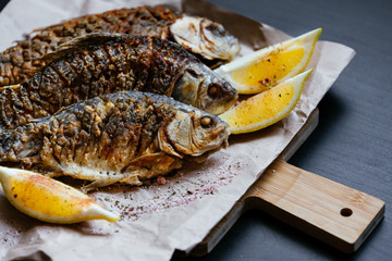 National dish of river fish. Grilled carp, crucian carp with lemon slices and salt on a wooden board and craft paper on a black wood background