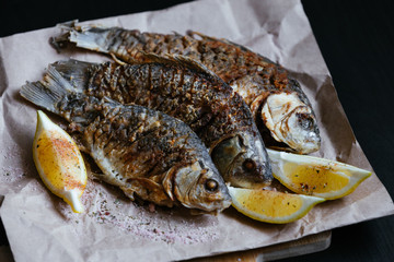 National dish of river fish. Grilled carp, crucian carp with lemon slices and salt on a wooden board and craft paper on a black wood background