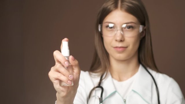 Doctor in goggles caucasian girl holds antiseptic in her hands and puts on her hands