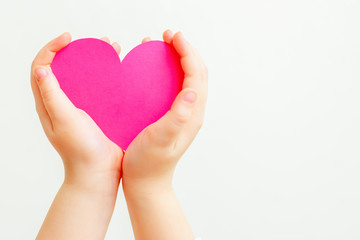 Closeup of hands of child holding paper pink heart on white background. Heart in hands with copy space.