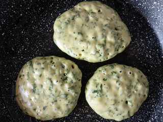 Top view on three pancakes with spinach cooking on frying pan