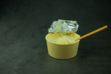 Soft butter with yellow spoon in yellow plastic container cup