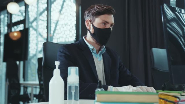 Serious man wear mask disinfects hands with antiseptic before working on computer workplace quarantine computer hygiene business office worker epidemic hygienic disinfection pandemic keyboard