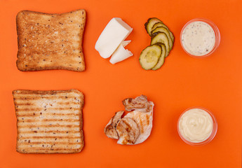 Ingredients for sandwich with chicken meat, mozzarella cheese and marinated cucumbers vegetable on trendy orange color background. Geometric Layout Ingredients composition. Top view. Flat lay