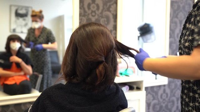 Hairdresser with security measures for the covid-19, new normality, social distance, with mask and plastic protective screen finishing the hairstyle to the client