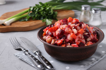 Traditional Russian salad vinaigrette with beets, carrots, potatoes and onions in a clay bowl against a gray concrete background, Vegetarian food, Closeup