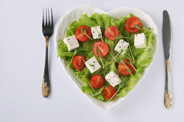 Healthy salad with cherry tomatoes, feta and peas microgreens on a heart-shaped plate on a white background, healthy eating day, Top view